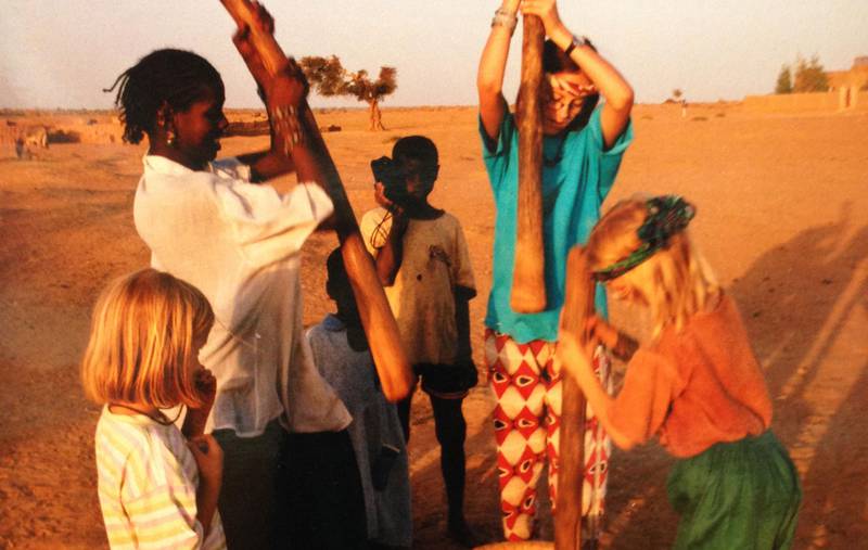 Bildet viser en ung Live Roaldseth Horsth som bodde i Mali på 1990-tallet. Hun har på seg en blå t-skjorte og jobber sammen med søsknene og folk fra Mali. Det ser ut som de knuser noe korn.