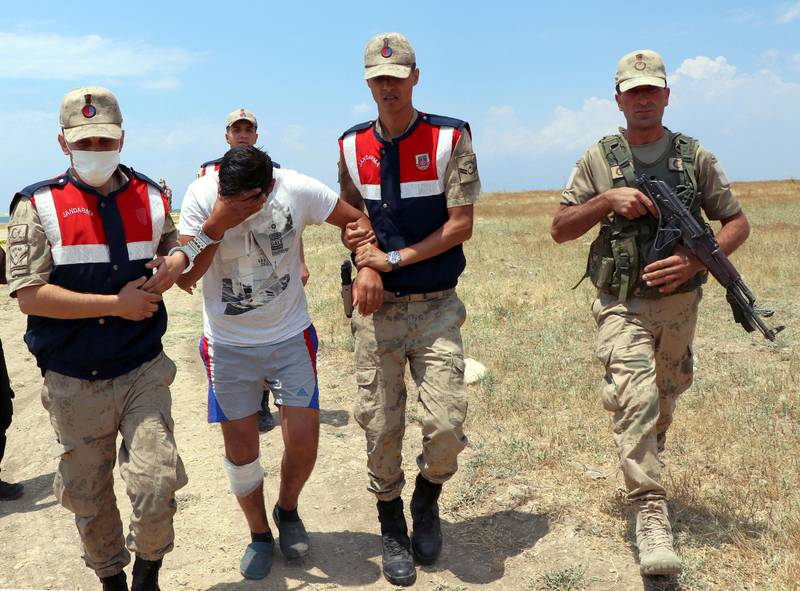 Bildet er av tre tyrkiske soldater i uniform. En bærer et gevær. To andre fører en mann uten uniform. Han er arrestert etter at båten med migranter sank.