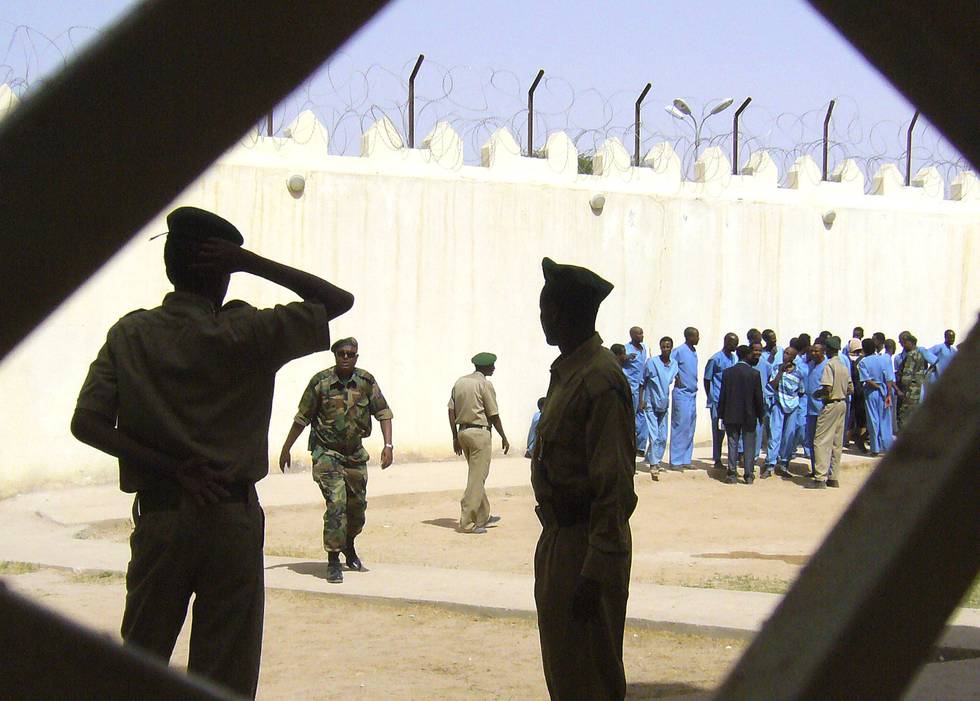 Bildet er av fangevoktere som ser ut i luftegården av et fengsel. Det er sand på bakken og lyse murer. I luftegården står det fanger i blå drakter. Arkivfoto: Katharine Houreld / AP / NTB