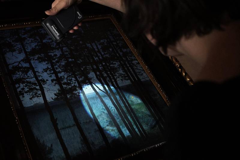 Bildet viser en ansatt som lyser etter skader på maleriet "Fiskerens Hytte"