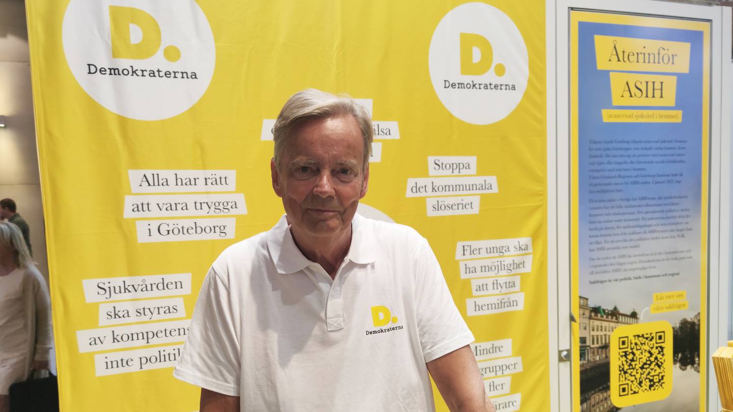 Bildet er av Rolf Sveen i partiet Demokraterna. Han har hvit trøye og står foran en valgbod som er farget gul og har logoer og lokale slagord. Foto: Arnfinn Storsveen / Klar Tale