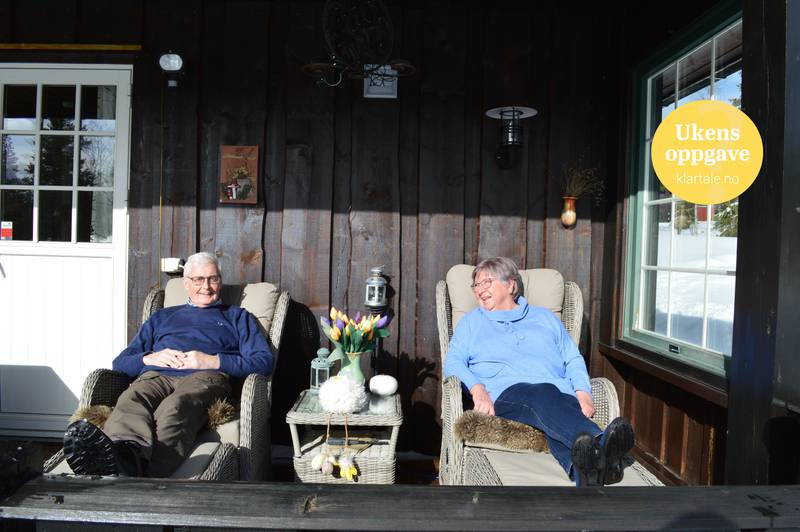 Bildet er av et eldre ektepar. De sitter i hver sin stol med støtte til beina. De sitter i sola på utsiden av hytta. De har solskinn i ansiktet.