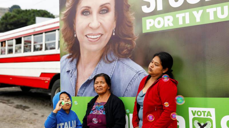 Bildet viser to kvinner og en gutt foran en buss med bilde av Sandra Torres på.