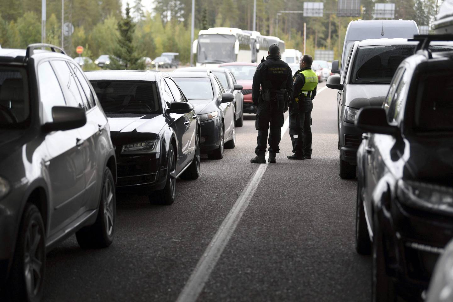 Biler står på rekke og rad på grensa inn til Finland. Mellom dem står to personer fra grensekontrollen. De sjekker bilene.