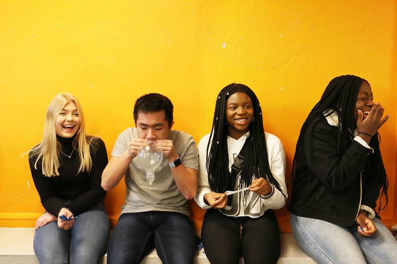 Bildet viser fire ungdommer som sitter og fikler med kondomer. Noen ler.