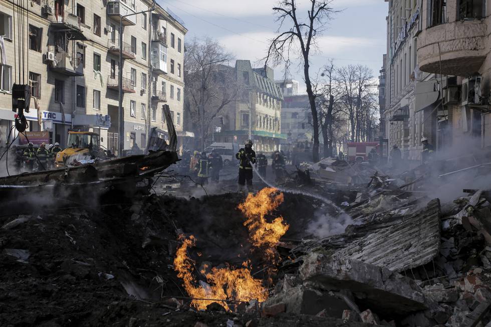 Bildet er av brannmannskaper som slokker en brann etter et russisk rakettangrep mot byen Kharkiv. I midten av bildet er det et krater med flammer. Det er svidd rundt omkring. Foto: AP / NTB