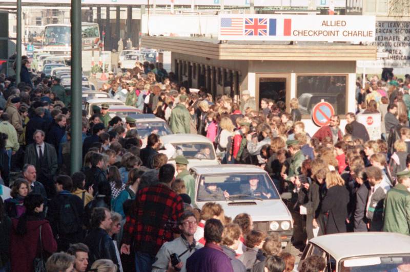 Bildet viser en stor mengde mennesker. De ser på biler som kjører forbi Checkpoint Charlie.