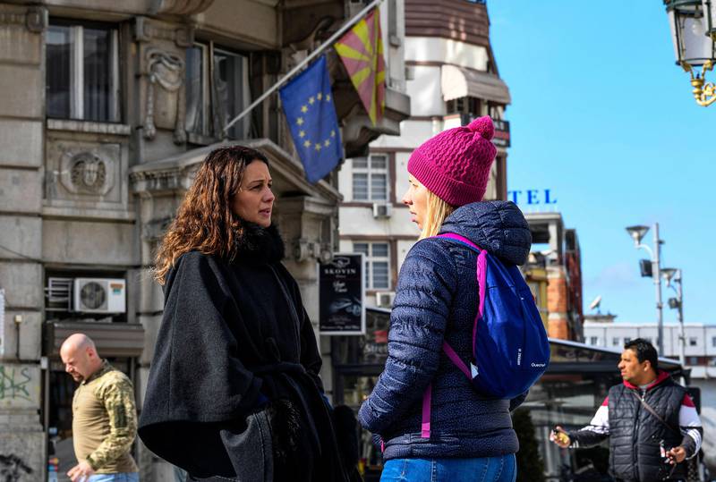 Bildet viser to kvinner som snakker sammen på gata. Flagget til EU og Makedonia henger i bakgrunnen.