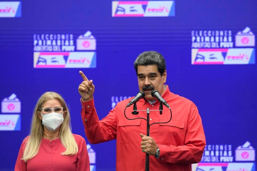 Bildet er av Venezuelas president Nicolás Maduro som snakker på en pressekonferanse. Han står bak et mikrofonstativ med to mikrofoner. Han er foran en blå vegg og har rød skjorte. Han har sort hår og bart. Ved siden av står en blond kvinne med briller og munnbind. Hun har på seg en rød trøye. Foto: Matias Delacroix / AP / NTB