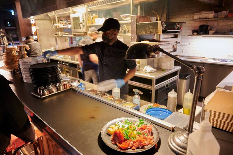 Bildet viser en kokk med munnbind som legger klar mat på en restaurant.
