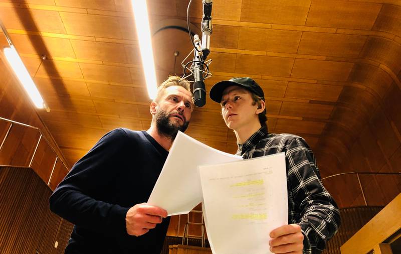 Bildet er av skuespillerne Espen Reboli Bjerke og Jonas Strand Gravli. De står foran en mikrofon som henger ned foran dem. De holder i hvert sitt ark med manus.