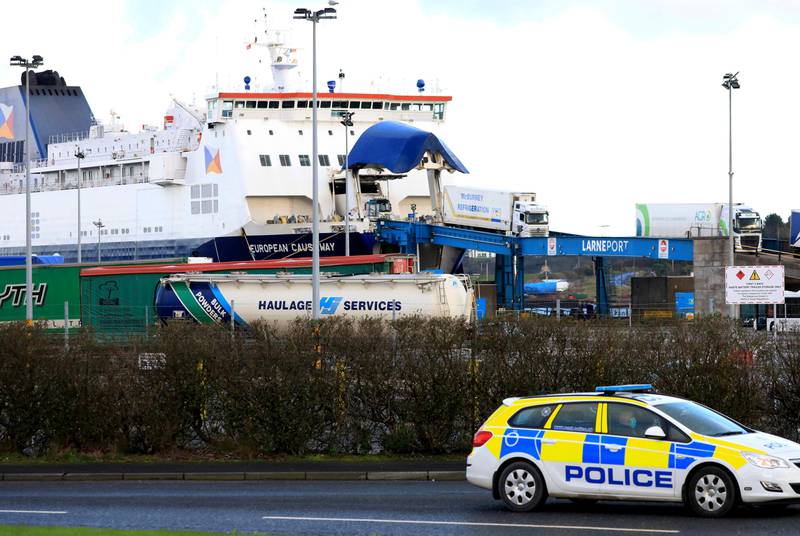 Bildet er av en ferje. Det står en politibil i forgrunnen. Det er et havneområde i Nord-Irland. En lastebil har kjørt iland.