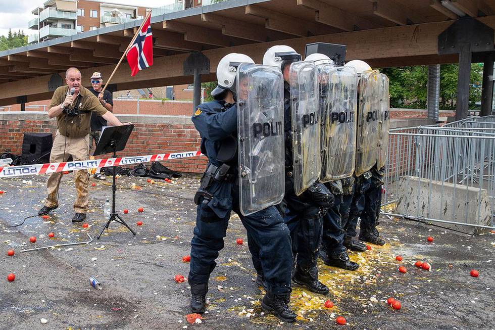 Bildet viser politi med skjold som beskytter Sian-leder Lars Thorsen mens han snakker. Folk har kastet egg og tomater mot dem. Det var da han snakket på Mortensrud i Oslo i sommer. 