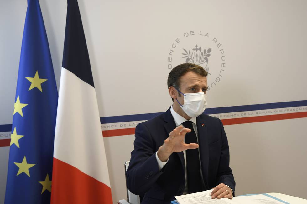 Bildet er av Frankrikes president Emmanuel Macron. Han sitter bak en pult mens han har på munnbind. Ett flagg fra Frankrike og ett flagg fra EU henger ved siden av ham. Foto: Nicolas Tucat / pool via AP / NTB