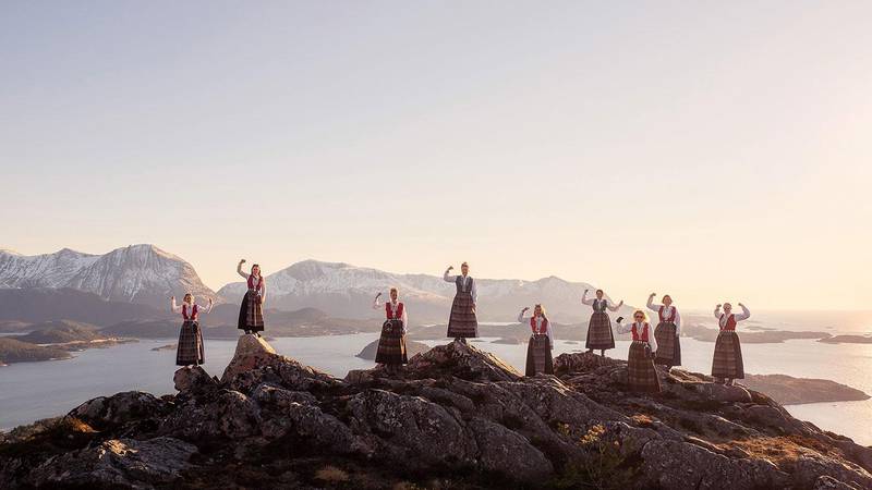 Bildet viser ni kvinner i bunad med knyttede never. De står på et berg med sjø og fjell i bakgrunnen. Bunadsgeriljaen kjemper for å beholde fødeavdelingen i Kristiansund.