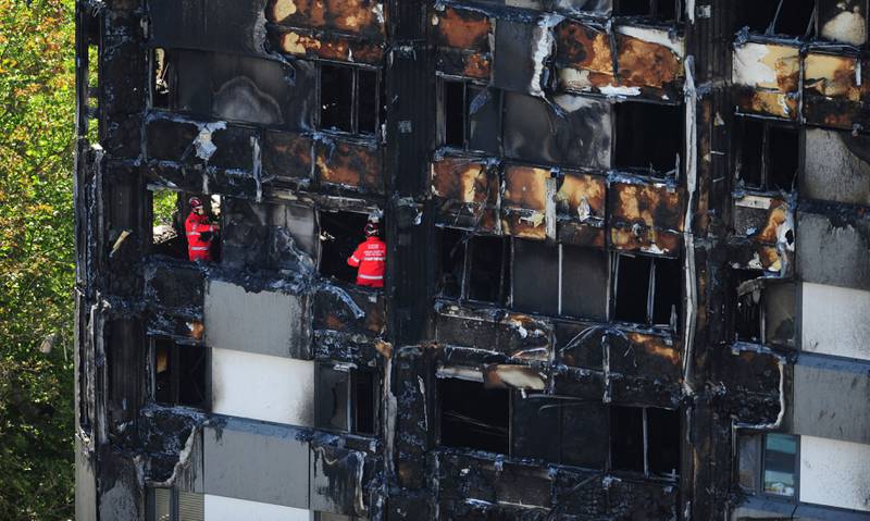 Bildet viser en utbrent blokk fra utsiden. I vinduene skimtes brannfolk som undersøker restene.