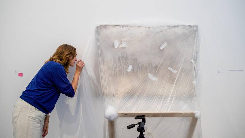Bildet viser utstillingsleder Charlotte T. Dølvik som sjekker bak plasten på et kunstverk.