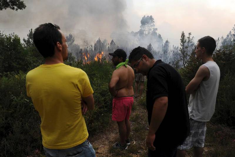 Bildet viser folk som ser på brannfolk. De ser bedrøvet ut. Det er mye røyk i bakgrunnen.