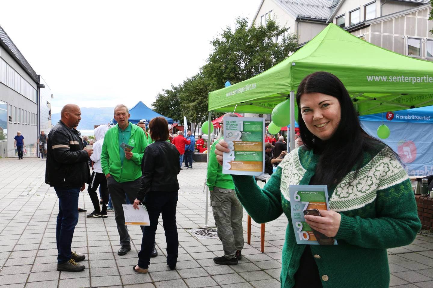 Bildet viser lærer Anne Blyseth i gågata i Mo i Rana. Hun er kledd i grønn jakke med Senterparti-logoer og holder opp en politisk brosjyre.
