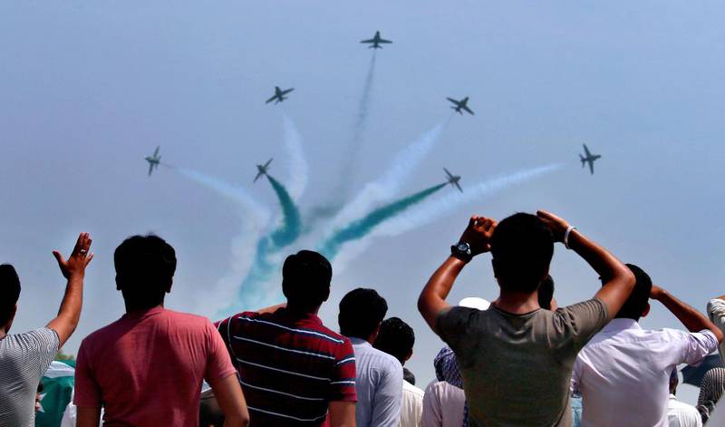 Bildet viser folk som ser på jagerfly. De lager røyk i fargene til Pakistans flagg.