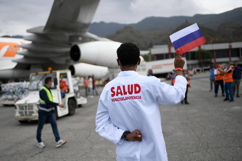 Bildet er av folk som tar last ut av et fly på en flyplass. En mann i hvit frakk holder opp et russisk flagg.
