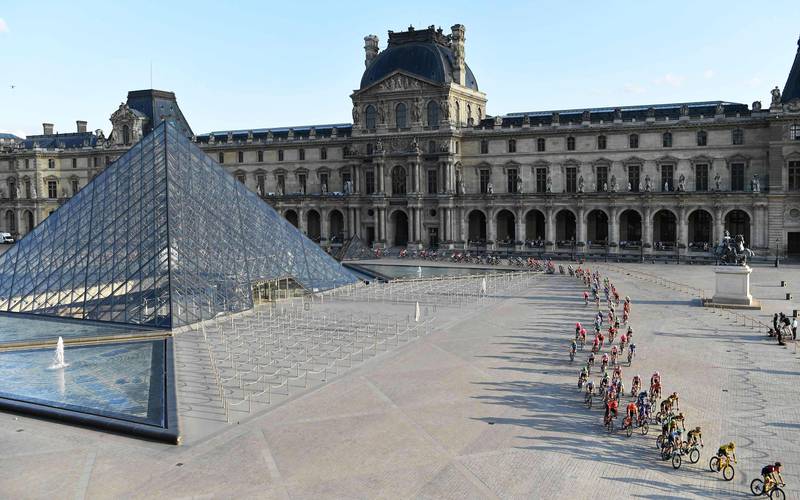 Bildet er tatt fra høyden i god avstand. Den viser mange syklister som kjører over plassen foran museet Louvre.