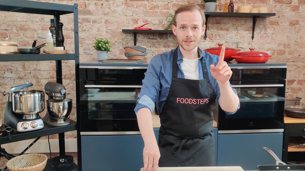 Jonas Modell står på et kjøkken. Bak han er en teglsteinvegg med ovner.