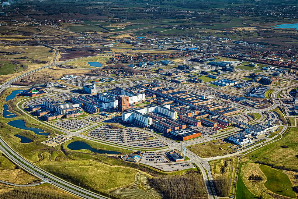 Bildet er et flyfoto av Aarhus Universitetshospital. Det er et stort område med mange bygninger og veier som går rundt området. Utenfor er det grøntområder. Foto: Aarhus Universitetshospital