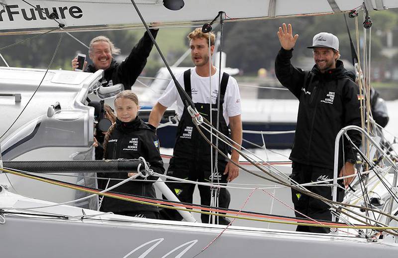 Bildet viser Greta Thunberg med faren og to kapteiner som vinker fra seilbåten.