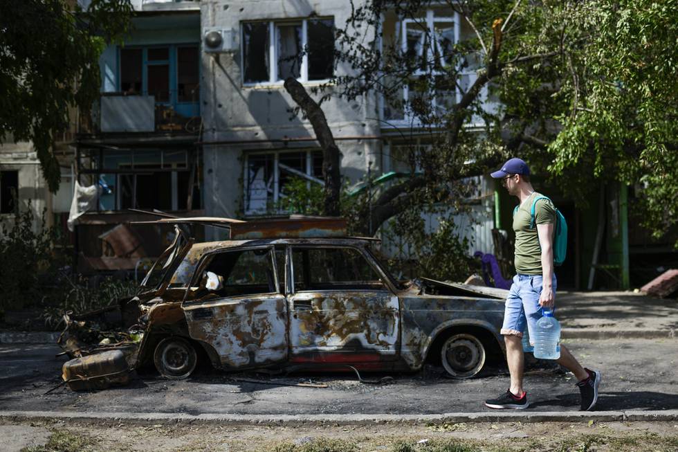 Bildet viser en mann som går med en vannbeholder forbi restene av en bil som ble ødelagt i et rakettangrep i Slavjansk 31. mai.
