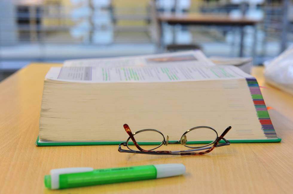 Bildet viser en pensumbok, briller og en tusj på en lesesal ved et universitet.
