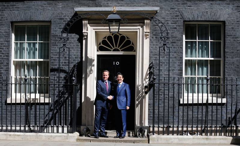 Bildet viser at David Cameron og statsminister Shinzo Abe fra Japan håndhilser foran statsministerboligen i Downing Street nummer 10. Katten Larry hviler til høyre i bildet.