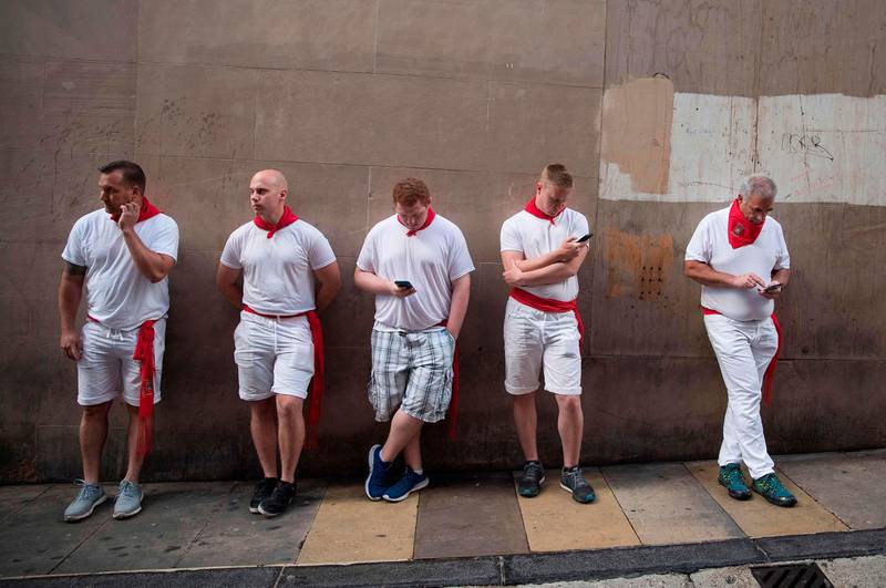 Bildet viser fem menn som lener seg mot en vegg. De er kledd i hvitt og har røde tørkler rundt halsen.