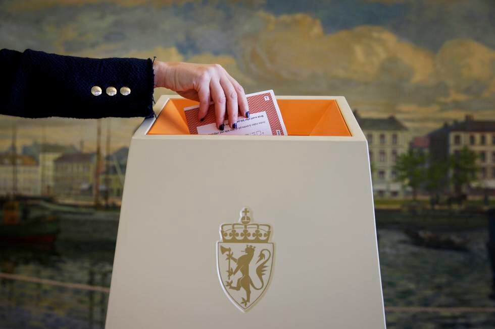 Bildet er av en arm som putter en stemmeseddel i en valgurne. I bakgrunnen er det en vegg med et påmalt bylandsskap. Foto: Håkon Mosvold Larsen / NTB / NPK
