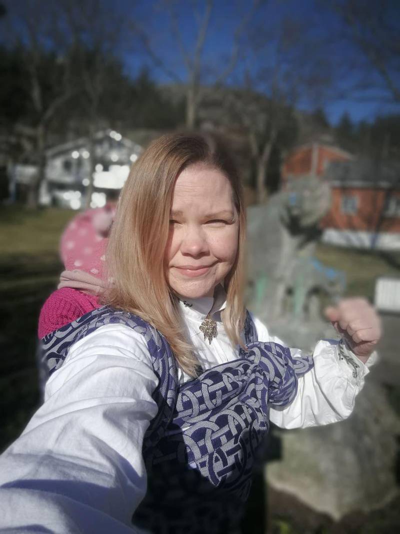 Bildet viser May-Britt Bjørke i bunad og med knyttet neve. Hun bærer datteren på ryggen i bæresjal.
