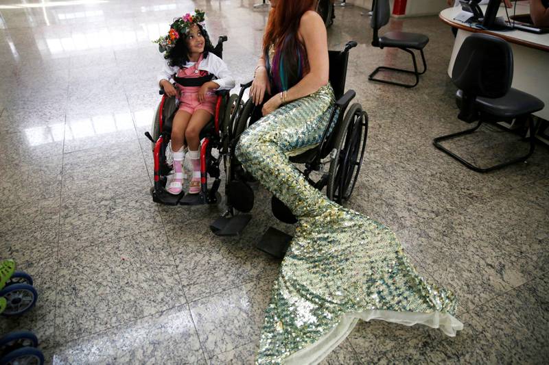 Bildet viser Carol Catan fra Brasil som snakker med en jente i rullestol. Catan er kledd ut som havfrue.