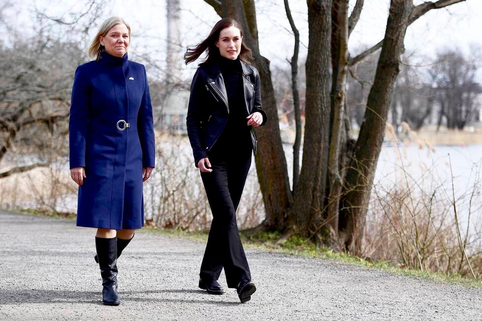 Bildet er av Magdalena Andersson (til venstre) og Sanna Marin som går på en sti ved vannet. Andersson har lyst hår og blå frakk. Hun er svensk statsminister. Marin har mørkt hår, mørk bukse og mørk jakke. Hun er finsk statsminister. Foto: Paul Wennerholm / EPA / NTB