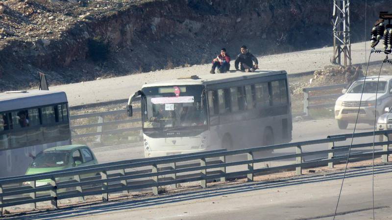 Bildet viser busser som forlater farlige Øst-Aleppo og andre byer rundt. To personer sitter på taket av bussen. 