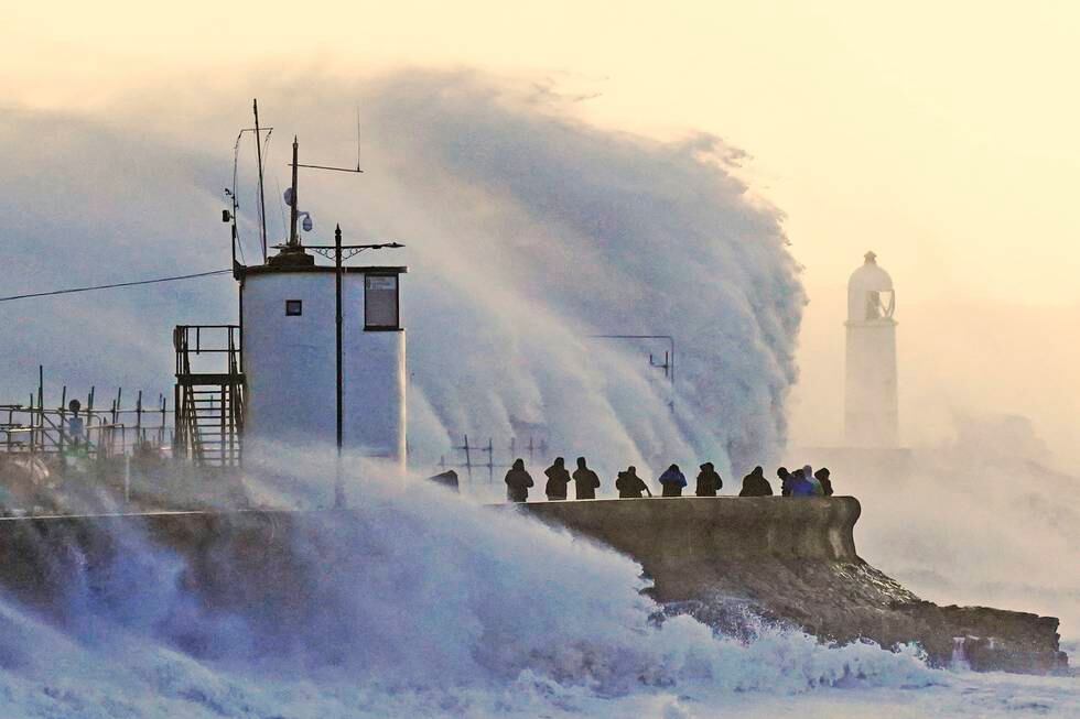 Bildet viser store bølger som fosser over et fyrtårn i Wales. Folk står rundt og ser på.