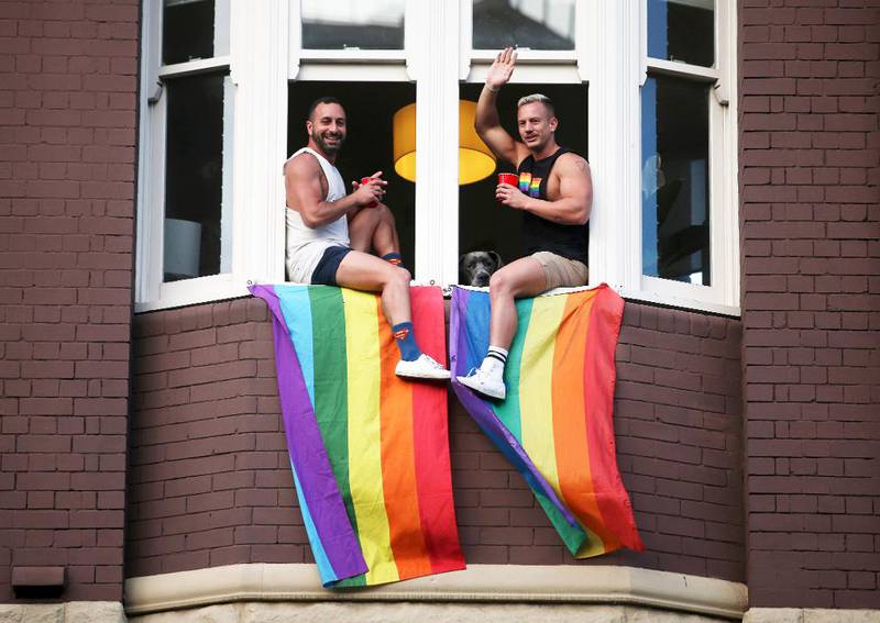 Bildet viser to menn som sitter i en vinduskarm med et homoflagg.