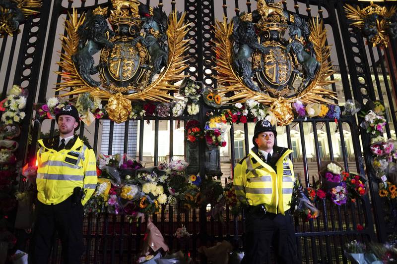 Politibetjenter står blant blomster og lapper som er blitt lagt ned utenfor Buckingham Palace etter nyheten om dronningens bortgang. Foto: Victoria Jones / PA via AP / NTB