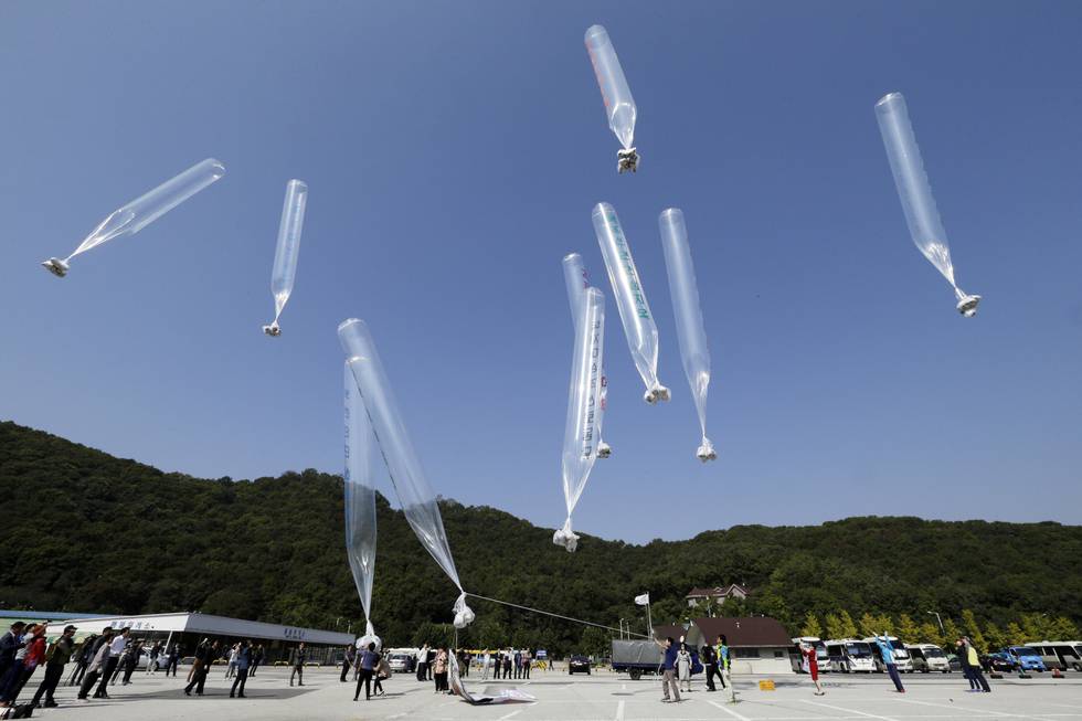 Bildet er av flere avlange ballonger med meldinger om hva som skjer i Nord-Korea. De blir sendt fra en stor asfaltert plass i Sør-Korea. Det står folk rundt omkring på bakken. Ahn Young-joon / AP / NTB