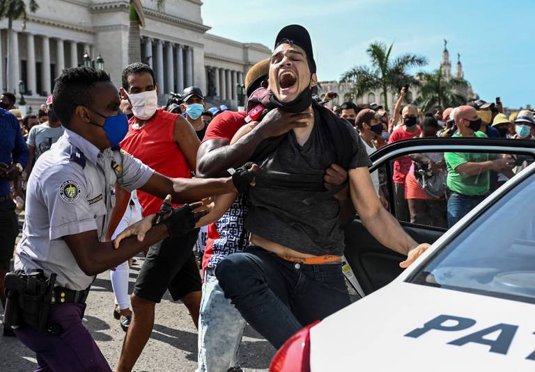 Bildet er av en ung mann som blir presset inn i en politibil under en protest på Cuba. Det er mye folk i bakgrunnen. Foto: Yamil Lage / AFP / NTB