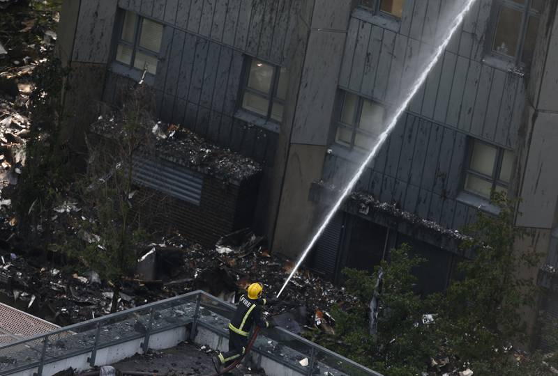 Bildet viser en brannmann som står og spyler vann på et bygg. 
