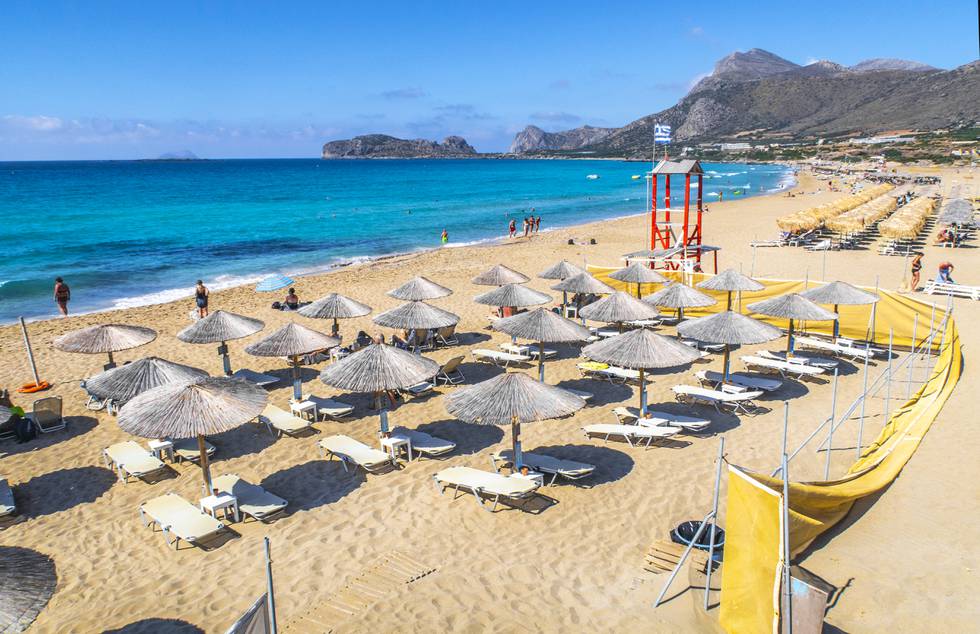 Bildet er av parasoller og solsenger på en strand. Det er blått hav. Bildet er fra Falasserna på Kreta i Hellas. Foto: Halvard Alvik / NTB