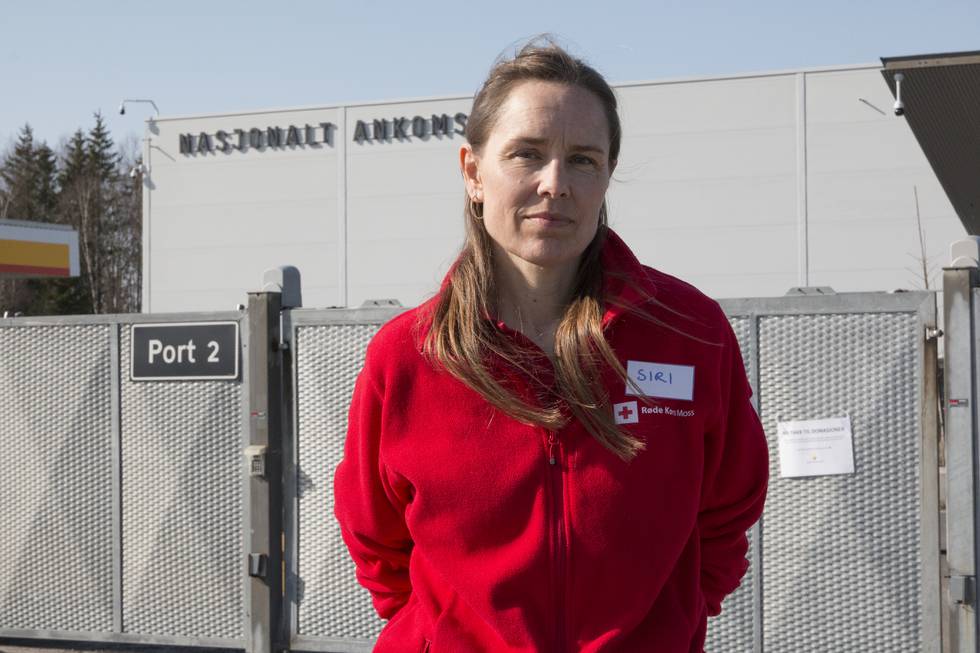 Bildet viser Siri Johansen foran det høye metallgjerdet utenfor Nasjonalt ankomstsenter. Hun har på seg en rød jakke med Røde Kors sin logo.