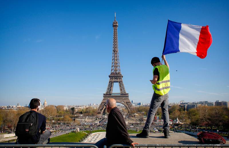 Bildet viser en mann med gul vest som veiver det franske flagget. Eiffel-tårnes sees i bakgrunnen.
