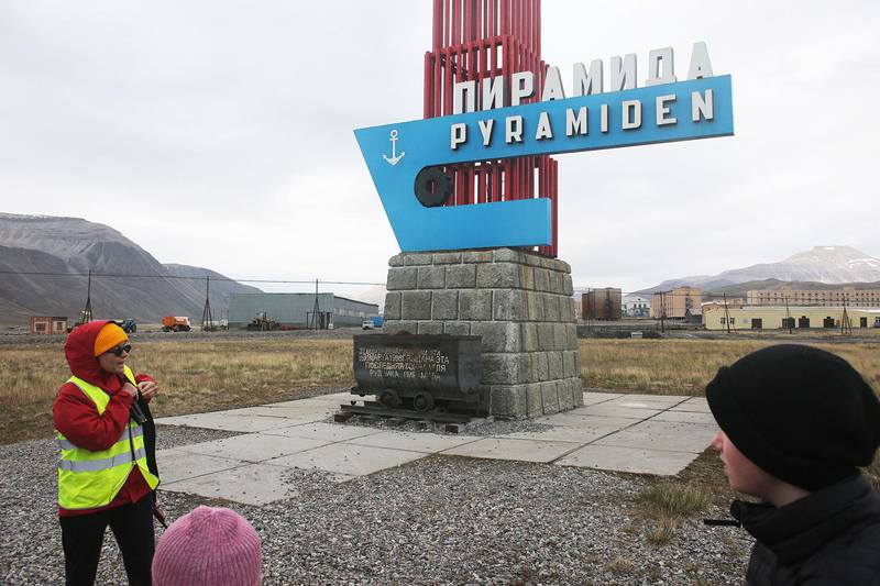 Bildet viser en guide foran skiltet til den russiske gamle gruvebyen Pyramiden på Svalbard.