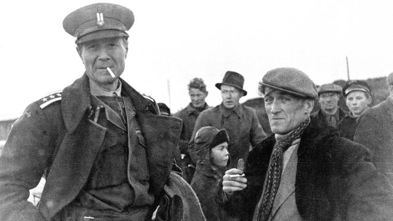 Bildet viser en militær person som røyker en sigarett. Han står sammen med en person i Sør-Varanger.