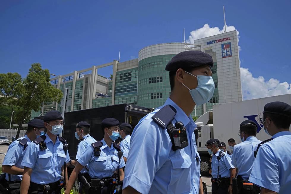 Bildet er av politi utenfor kontorene til avisa Apple Daily i Hongkong. De har lyseblå uniformer, mørkeblå bereter og lyseblå munnbind. Bildet er fra 17. juni, da sjefredaktøren og fire andre ansatte i avisa ble pågrepet. Foto: Kin Cheung / AP / NTB